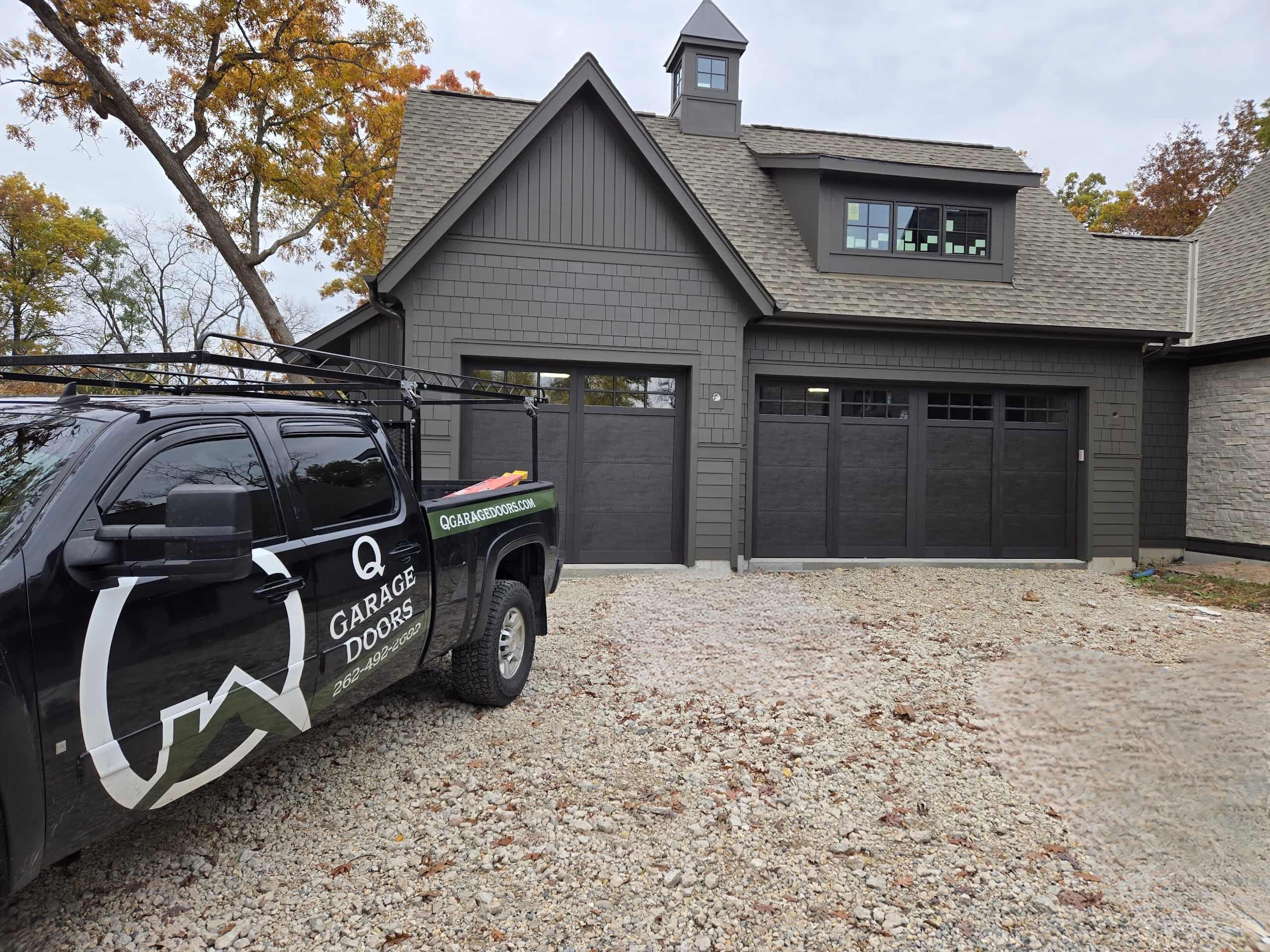 Twin black carriage-house garage doors on a custom Wisconsin home, Q Garage Doors truck in the driveway
