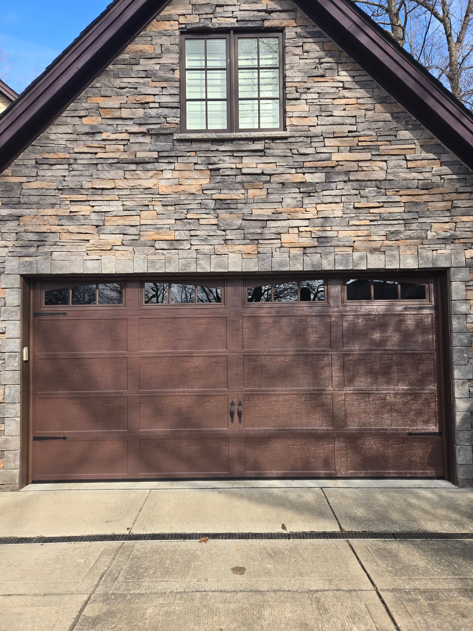 Mahogany carriage-house garage door beneath a stacked-stone gable