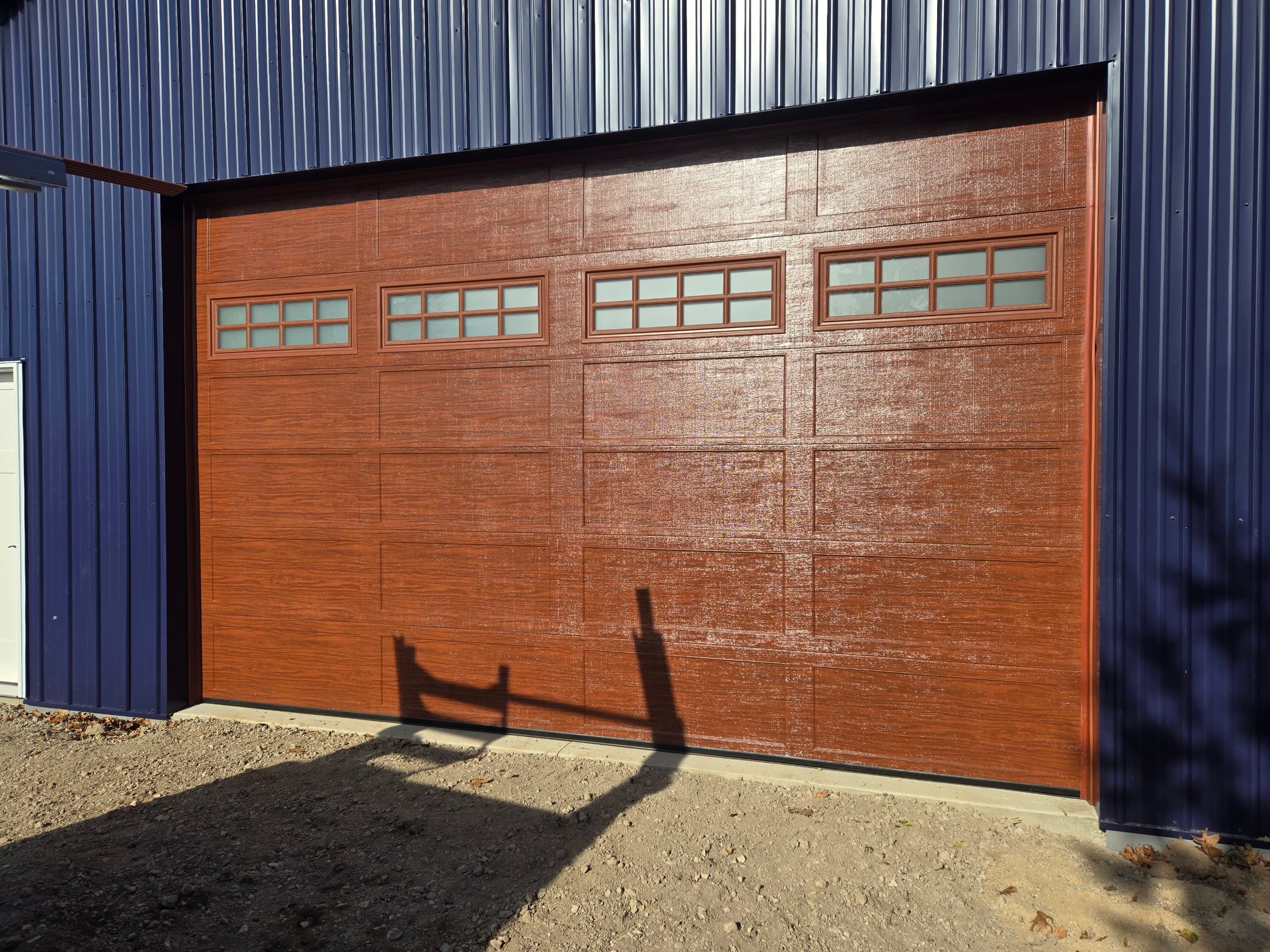 Wood-grain garage door with frosted window row on a blue pole building