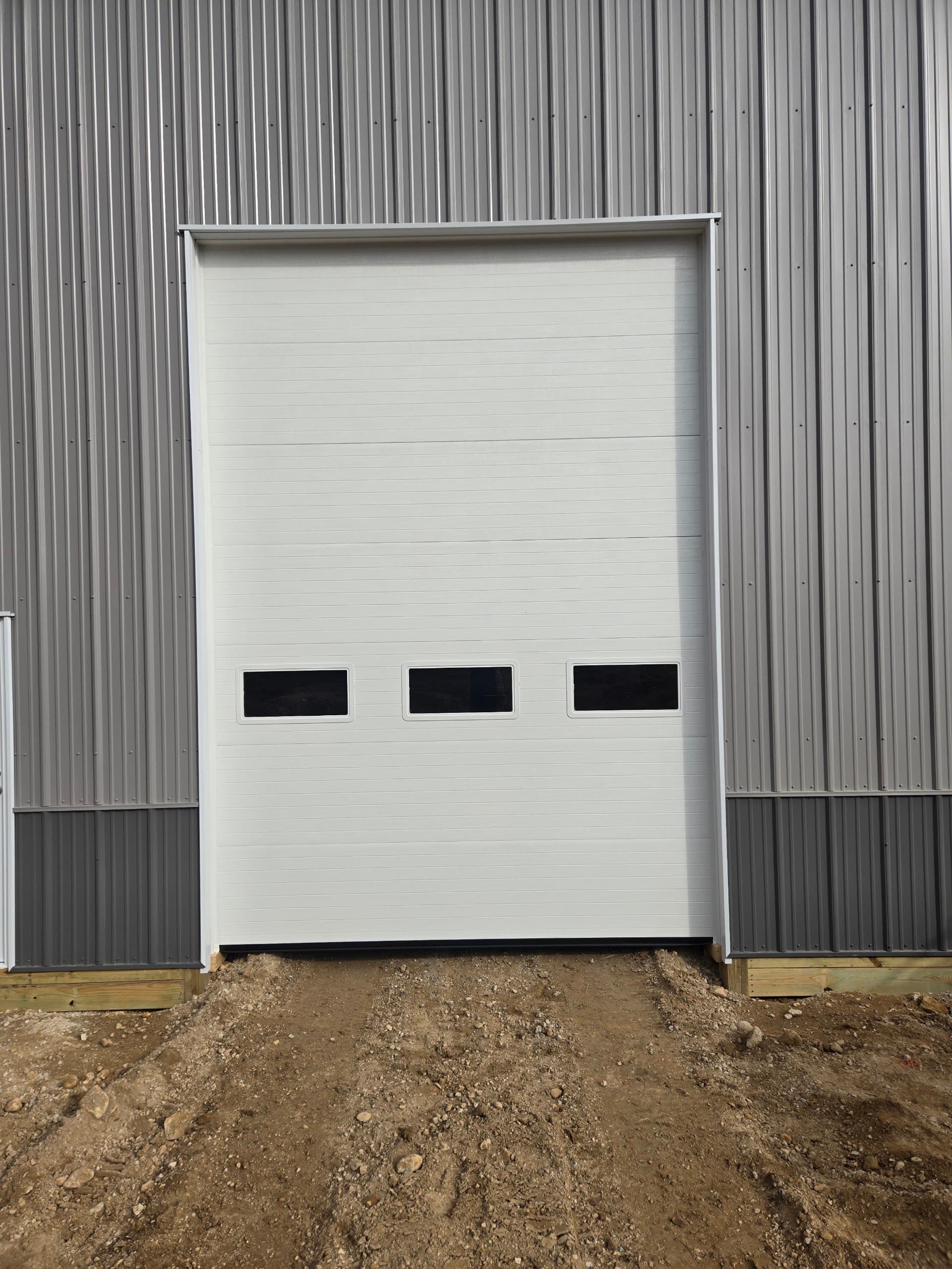 Tall white insulated commercial overhead door on a metal workshop