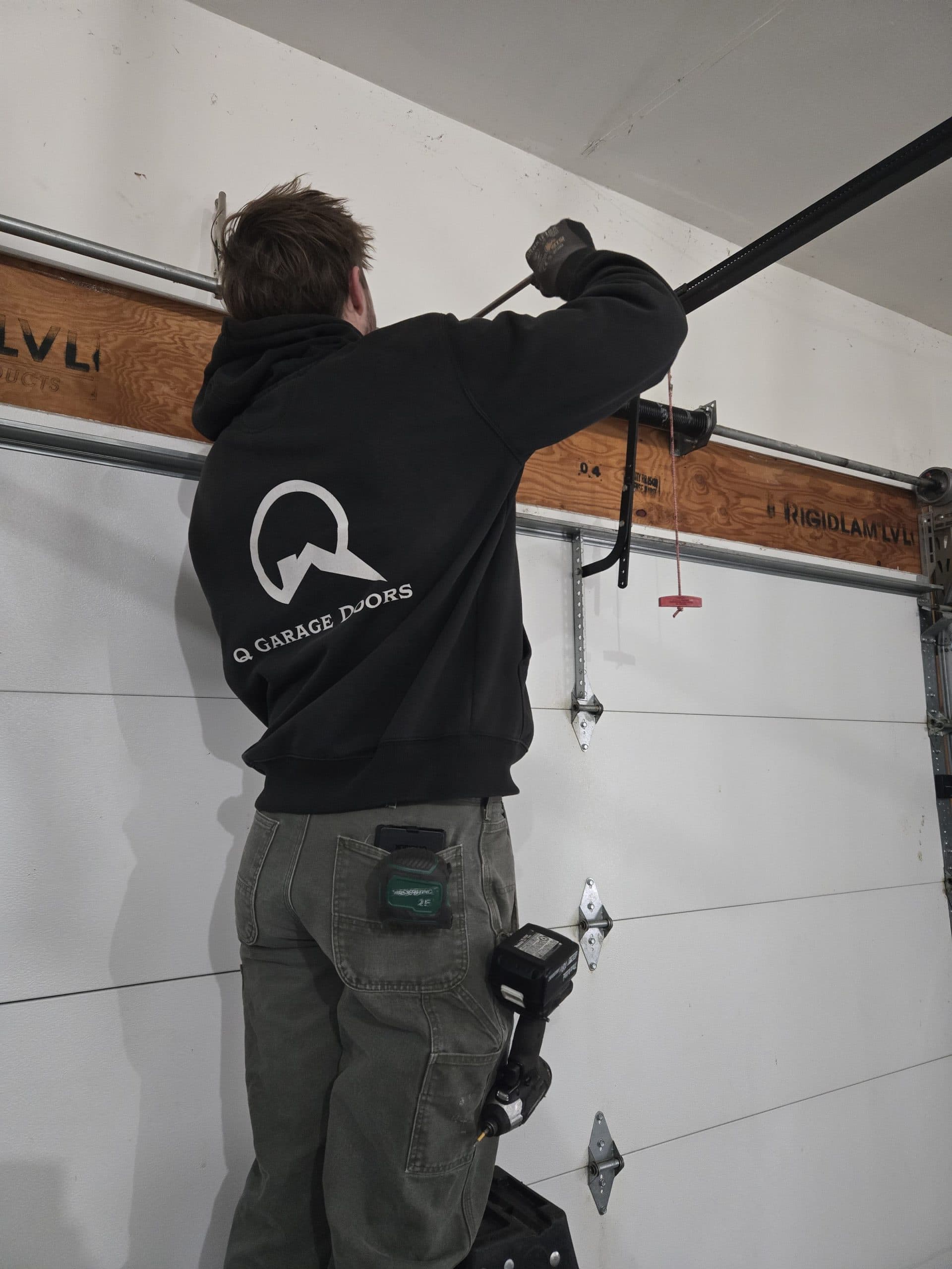 Noah Quernemoen balancing a garage door spring, Q Garage Doors logo on his back